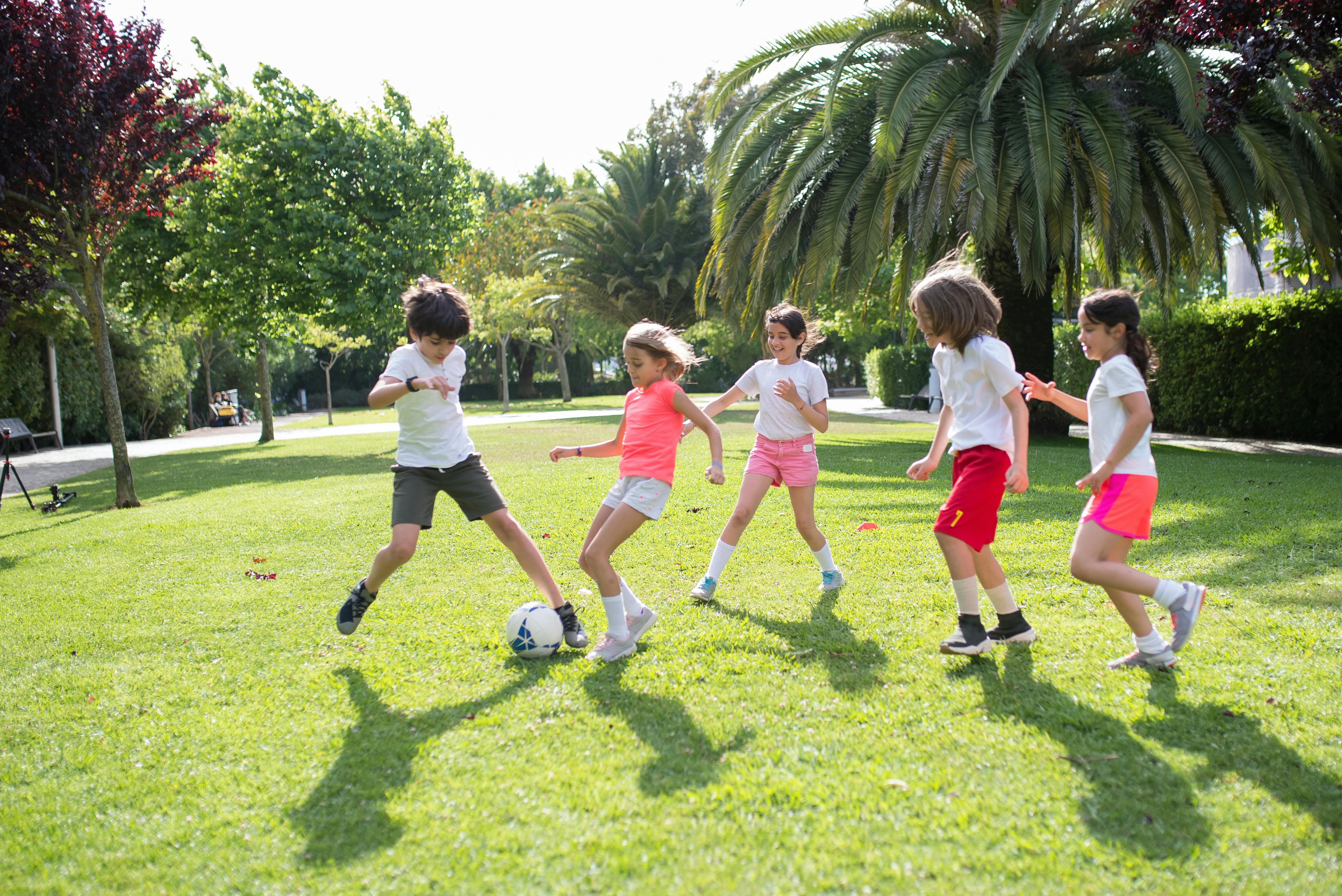 Children playing football together in a sunny park